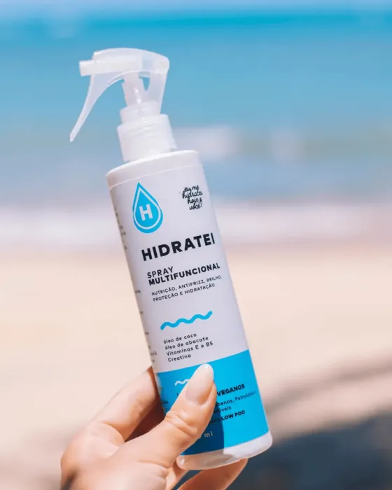 Mão segurando o Spray Leave-in Multifuncional da Hidratei na praia